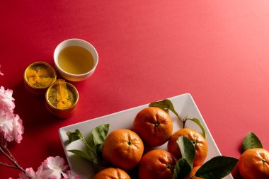 Kırmızı arka planda kiraz çiçeği ve portakalların yakın plan kompozisyonu. Çin yeni yılı, gelenek ve kutlama konsepti.