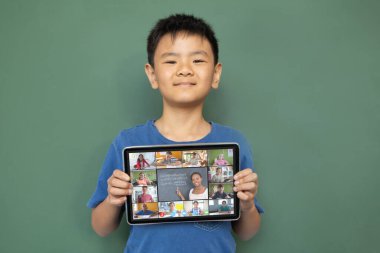 Çeşitli ilkokul öğrencileriyle video görüşmesi için elinde tablet olan gülümseyen Asyalı çocuk. iletişim teknolojisi ve çevrimiçi eğitim, dijital kompozit resim.