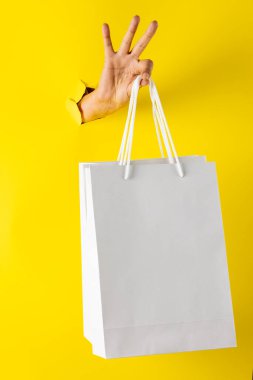 Sarı arka planda el ele alışveriş torbalarının kompozisyonu. Perakende, alışveriş ve Kara Cuma konsepti.