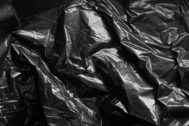 Kırışıklıklar ve kıvrımlar üzerindeki ışığı ve gölgeyi siyah plastik kaplamayla yansıtıyor. monokrom ışık ve doku, soyut arkaplan resmi.