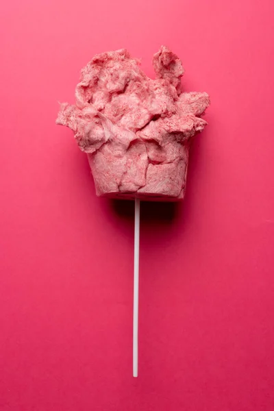 Vertical image of homemade pink candy floss on stick, on pink background with copy space. Tasty home made sweet foods.