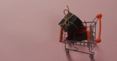 Kutuları olan alışveriş arabasının videosu ve pembe arka planda fotokopi alanı. Siber Pazartesi, Kara Cuma, perakende, alışveriş ve tasarruf kavramı.