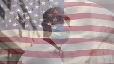 Amerikan bayrağının şehir caddesinde maskeli Afro-Amerikan bir adamın üzerinde dalgalanmasının animasyonu. covid 19 salgın konsepti boyunca dijital olarak üretilen küresel sağlık önlemleri.