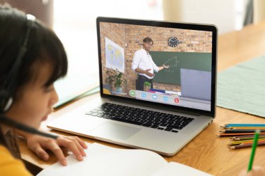 Görüntülü konuşma için dizüstü bilgisayar kullanan Asyalı bir kız. Ekranda melez erkek öğretmen var. iletişim teknolojisi ve çevrimiçi eğitim, dijital kompozit resim.