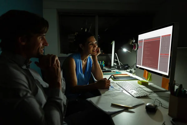 Two diverse male and female colleagues sitting at desk and using computer with coding on screen. coding, programming and computer technology digital composite image.