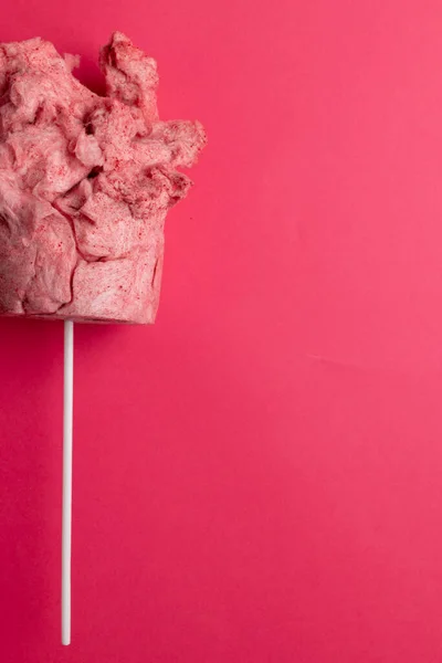 Vertical image of homemade pink candy floss on stick, on pink background with copy space. Tasty home made sweet foods.