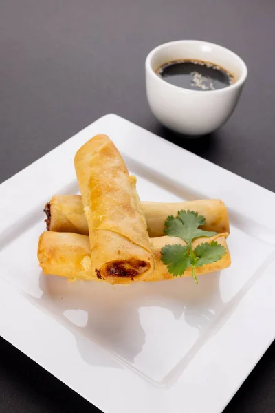Close up of asian spring rolls on white plate and soy sauce on grey background. Asian tasty home cooked food and healthy eating.