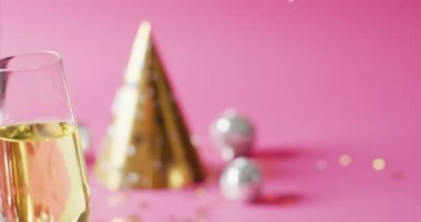 Altın parti şapkalı ve pembe arka planda takılar olan şampanya kadehinin videosu. Yeni yıl partisi ve kutlama konsepti.