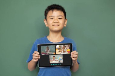 Çeşitli ilkokul öğrencileriyle video görüşmesi için elinde tablet olan gülümseyen Asyalı çocuk. iletişim teknolojisi ve çevrimiçi eğitim, dijital kompozit resim.