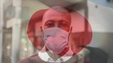 Afro-Amerikan adam üzerinde sallanan Japon bayrağının animasyonu. Şehir caddesinde maske takıyor. covid 19 salgın konsepti boyunca dijital olarak üretilen küresel sağlık önlemleri.