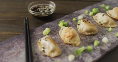 Tabakta gyoza köftesi ve soya sosuyla ahşap arka planda yemek çubukları var. Yiyecek, içecek ve renk konsepti.