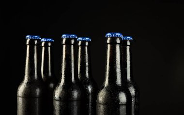 Siyah arka planda kopyalama alanı olan mavi kapaklı altı bira şişesi resmi. Alkol, içecek ve bira günü kutlamaları..