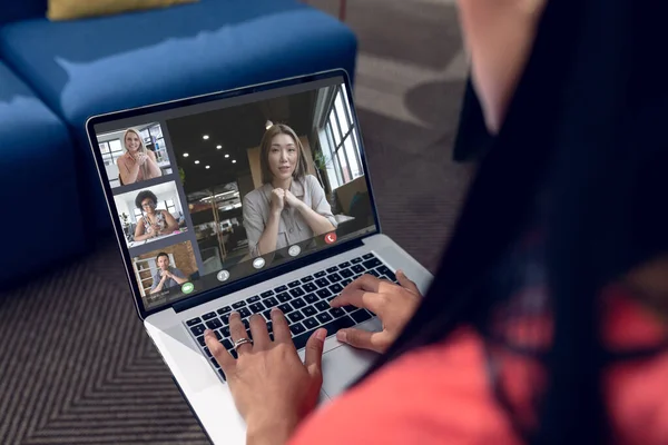 Over shoulder view of biracial businesswoman making laptop video call, diverse colleagues on screen. Business communication, inclusivity, flexible working and digital interface concept.