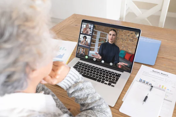 Senior caucasian businesswoman at desk making laptop video call with diverse colleagues on screen. Business communication, flexible working and digital interface concept.