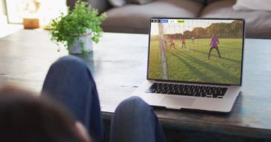 Farklı erkek futbol oyuncularının ekranda oynadığı dizüstü bilgisayar kullanan bir adam. Küresel spor kavramı, dijital kompozit video.
