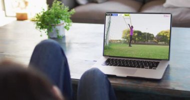 Ekranda maç yapan Afrikalı Amerikalı erkek futbolcuyla dizüstü bilgisayar kullanan bir adam. Küresel spor kavramı, dijital kompozit video.