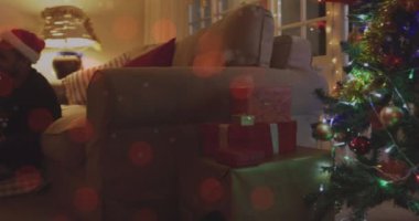 Noel Baba şapkalı, gitar çalan ve Noel 'de şarkı söyleyen beyaz bir çiftin üzerinde ışık lekeleri. Noel, müzik, gelenek ve kutlama konsepti dijital olarak oluşturuldu.