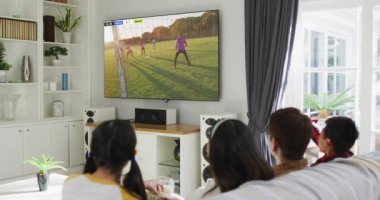 Asyalı bir aile televizyonda çeşitli erkek futbol oyuncularıyla maç izliyor. Küresel spor kavramı, dijital kompozit video.