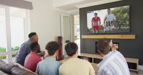 Różnorodni Przyjaciele Wspierający Oglądający Telewizję Różnymi Męskimi Piłkarzami Grającymi Mecz — Wideo stockowe