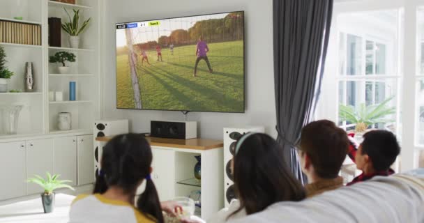 多様な男性サッカー選手とのアジアの家族のテレビを見て画面上で一致を果たしている グローバルスポーツの概念 デジタル複合ビデオ — ストック動画