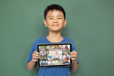 Gülümseyen Asyalı çocuk ekranda çeşitli gülümseyen lise öğrencileriyle video çağrısı için tablet tutuyor. iletişim teknolojisi ve çevrimiçi eğitim, dijital kompozit resim.