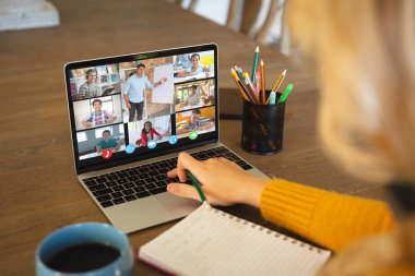 Beyaz bir kadın ekranda çeşitli ilkokul öğrencilerinin gülümsediği bir video görüşmesi için dizüstü bilgisayar kullanıyor. iletişim teknolojisi ve çevrimiçi eğitim, dijital kompozit resim.