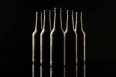 Siyah arka planda kopya alanı olan mavi kapaklı beş bira şişesi resmi. Alkol, içecek ve bira günü kutlamaları..