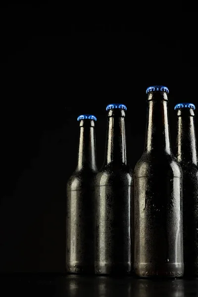 Вертикальное Изображение Четырех Тёмных Стеклянных Бутылок Пива Голубыми Колпачками Чёрном — стоковое фото