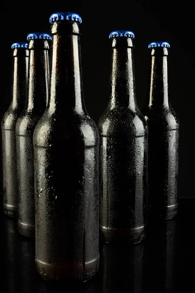 Image of five beer bottles with blue crown caps, with copy space on black background. Drinking alcohol, refreshment and lager day celebration concept.