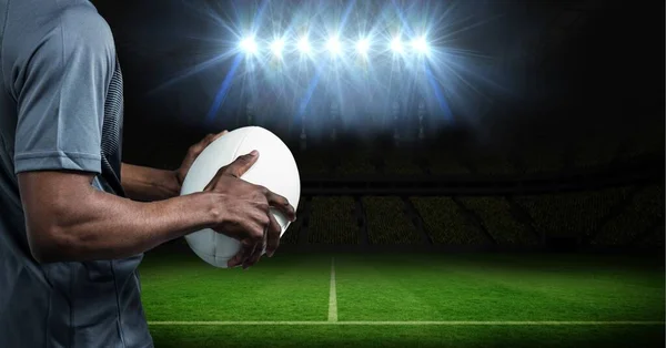 Composition of male rugby player holding rugby ball over sports stadium. sport and competition concept digitally generated image.