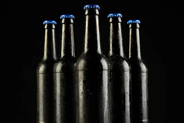 Image of five beer bottles with blue crown caps, with copy space on black background. Drinking alcohol, refreshment and lager day celebration concept.