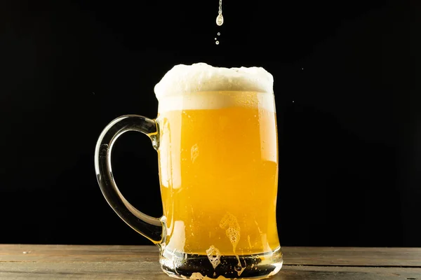 Image of beer pouring into glass tankard of foamy beer on wooden table, with copy space. Drinking alcohol, refreshment and lager day celebration concept.