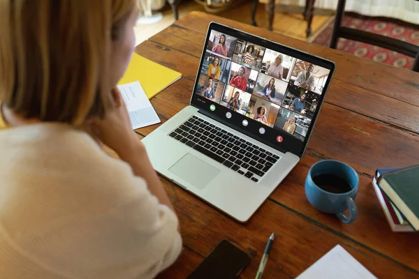 Asian businesswoman at table making laptop video call with diverse colleagues on screen. Business communication, flexible working and digital interface concept.