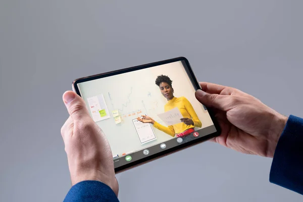 Hands of caucasian businessman making video call on tablet with diverse female colleague on screen. Business communication, flexible working, inclusivity and digital interface concept.