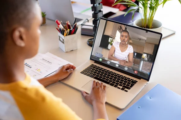 African american woman at desk making laptop video call with female colleague on screen. Business communication, flexible working, inclusivity and digital interface concept.