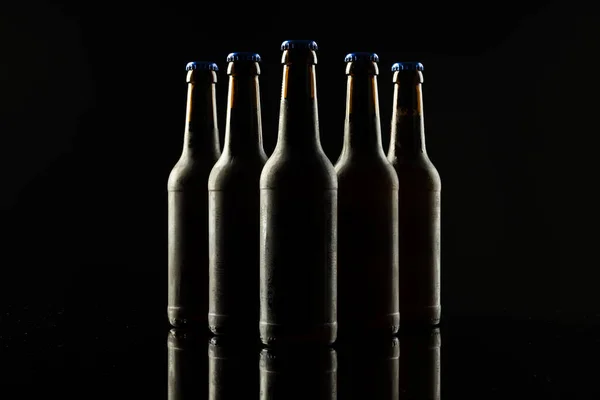 Image of five beer bottles with blue crown caps, with copy space on black background. Drinking alcohol, refreshment and lager day celebration concept.