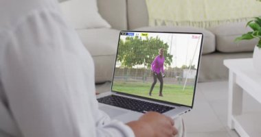 Ekranda maç yapan Afrikalı Amerikalı erkek futbolcunun dizüstü bilgisayarını kullanan eller. Küresel spor kavramı, dijital kompozit video.
