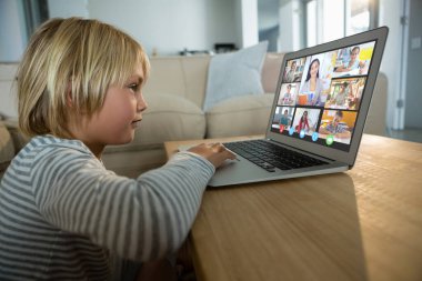 Beyaz çocuk ekranda çeşitli ilköğretim öğrencileri gülümserken görüntülü konuşma için laptop kullanıyor. iletişim teknolojisi ve çevrimiçi eğitim, dijital kompozit resim.