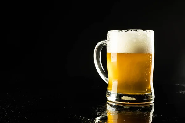 Image of pint glass tankard of foamy beer, with copy space on black background. Drinking alcohol, refreshment and lager day celebration concept.