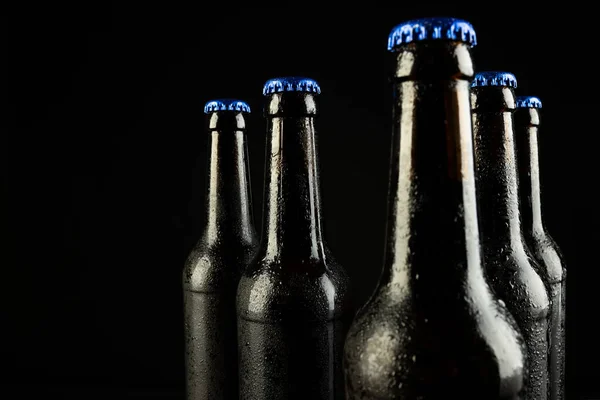 Image of five beer bottles with blue crown caps, with copy space on black background. Drinking alcohol, refreshment and lager day celebration concept.