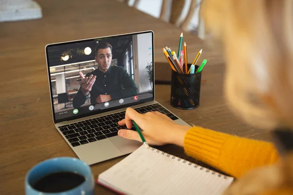 Caucasian businesswoman at table making laptop video call with caucasian male colleague on screen. Business communication, flexible working and digital interface concept.