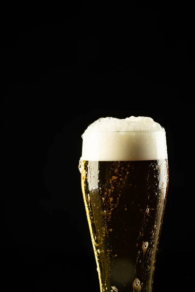 Image of full pint glass of foamy beer, with copy space on black background. Drinking alcohol, refreshment and lager day celebration concept.