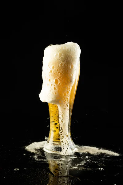 Image of overflowing pint glass of foamy beer, with copy space on black background. Drinking alcohol, refreshment and lager day celebration concept.