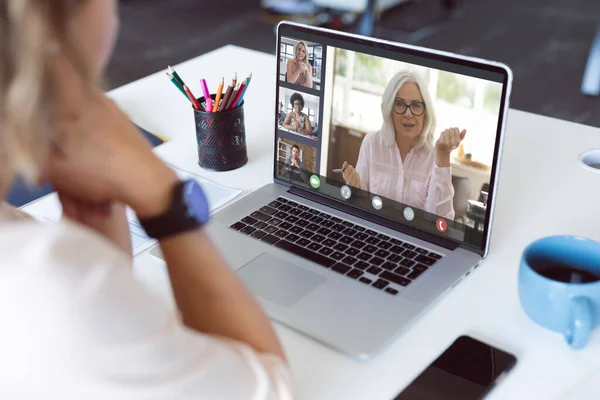 Caucasian businesswoman at desk making laptop video call with diverse colleagues on screen. Business communication, flexible working and digital interface concept.