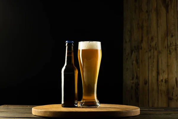 Image of full bottle and pint glass of beer on wooden table, with copy space. Drinking alcohol, refreshment and lager day celebration concept.