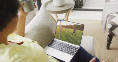 Ekranda maç yapan çeşitli erkek futbolcularla birlikte dizüstü bilgisayar kullanan Afro-Amerikalı bir kadın. Küresel spor kavramı, dijital kompozit video.