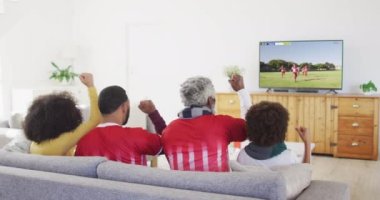 Ekranda maç yapan çeşitli erkek futbol oyuncularıyla televizyon izleyen Afro-Amerikan ailesi. Küresel spor kavramı, dijital kompozit video.