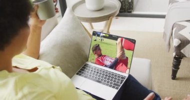 Ekranda maç yapan çeşitli erkek futbolcularla birlikte dizüstü bilgisayar kullanan Afro-Amerikalı bir kadın. Küresel spor kavramı, dijital kompozit video.