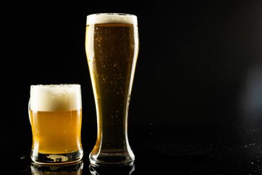 Büyük bardak ve köpüklü biranın resmi, siyah arka planda fotokopi alanı var. Alkol, içecek ve bira günü kutlamaları..