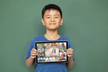Gülümseyen Asyalı çocuk ekranda çeşitli gülümseyen lise öğrencileriyle video çağrısı için tablet tutuyor. iletişim teknolojisi ve çevrimiçi eğitim, dijital kompozit resim.